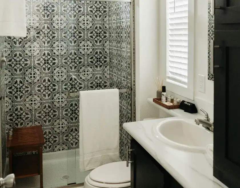 Modern bathroom with patterned tile wall, white sink, and window blinds.
