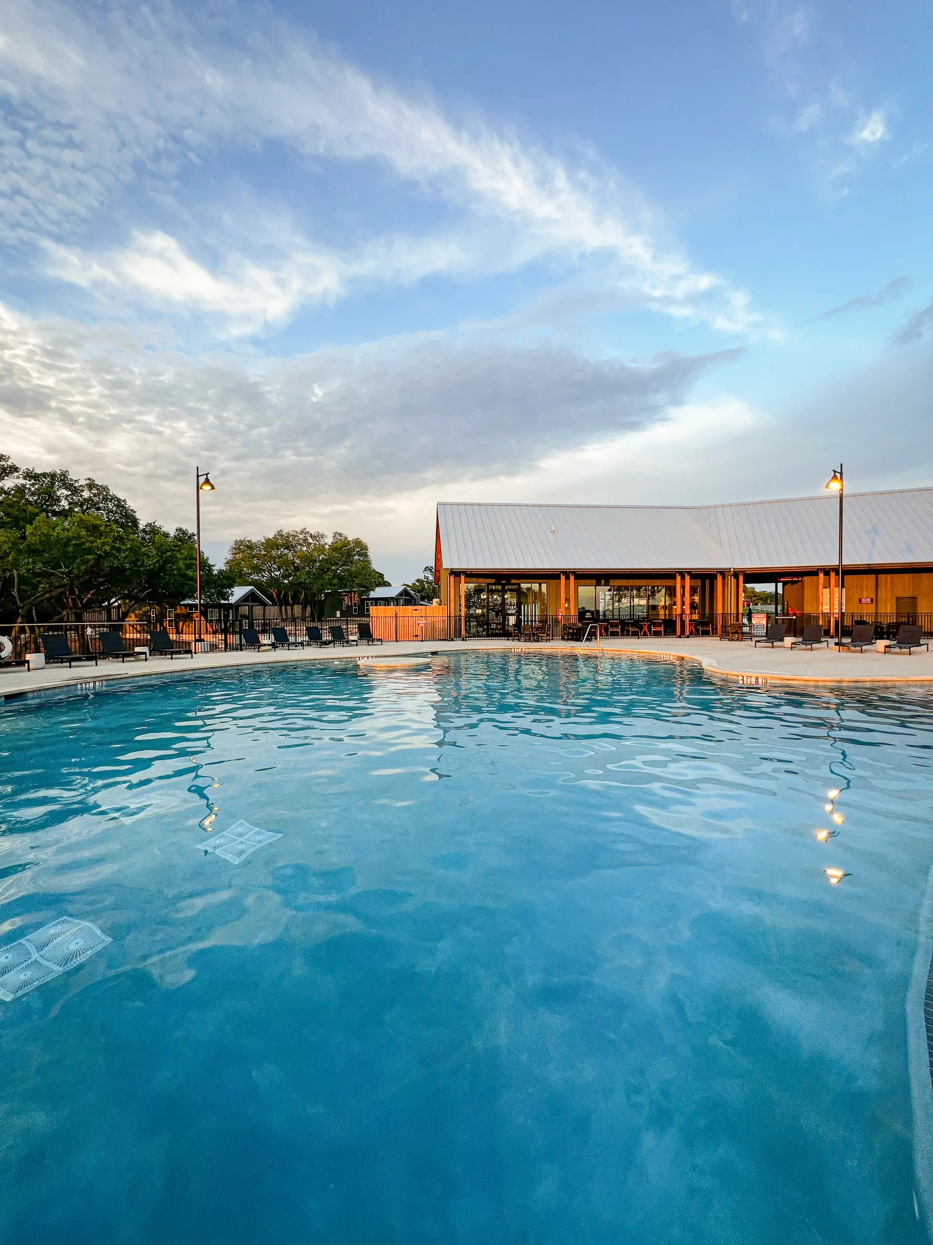 Resortstyle pool at dusk with the amenity center behind it at Horseshoe Ridge RV Resort in Wimberley, TX