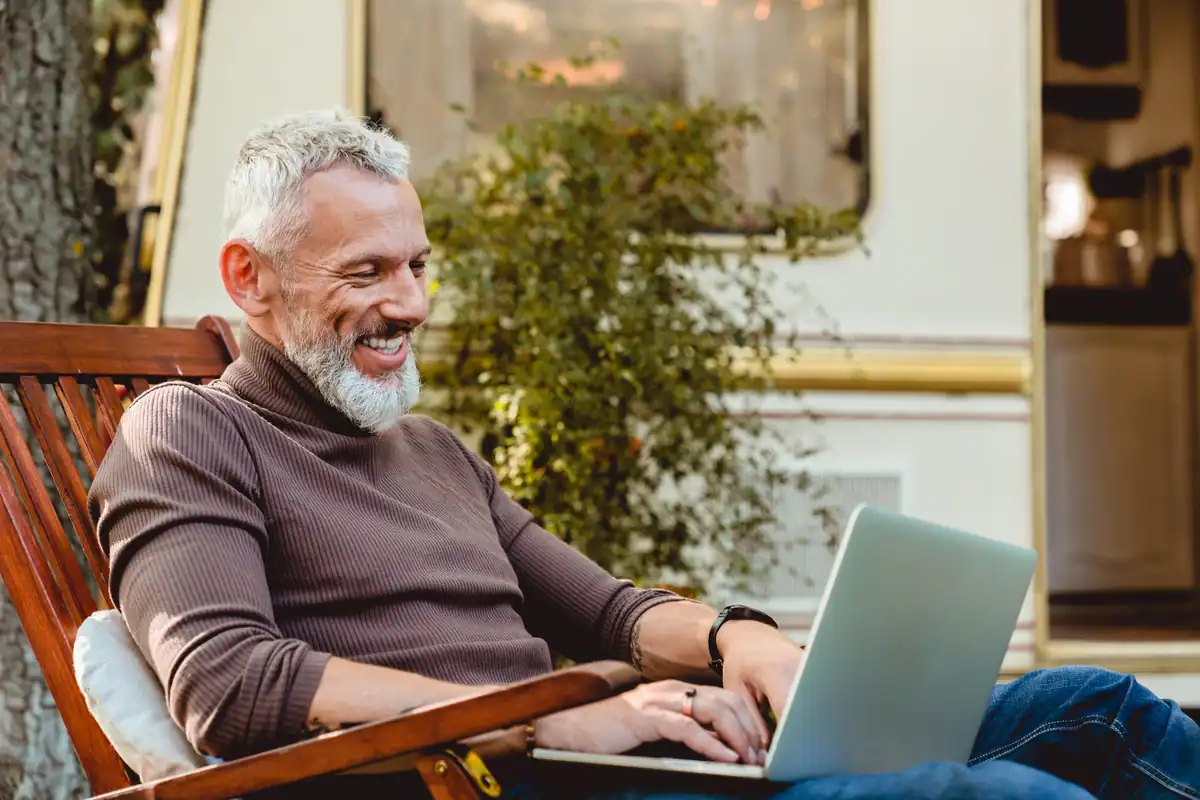 Smiling RVer relaxing with a laptop in a chair outside his RV at a Texas Hill Country resort