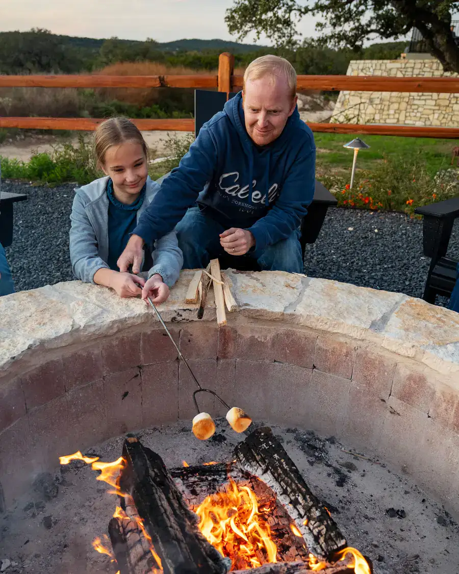Father and daughter roasting marshmallows over a stone fire pit
