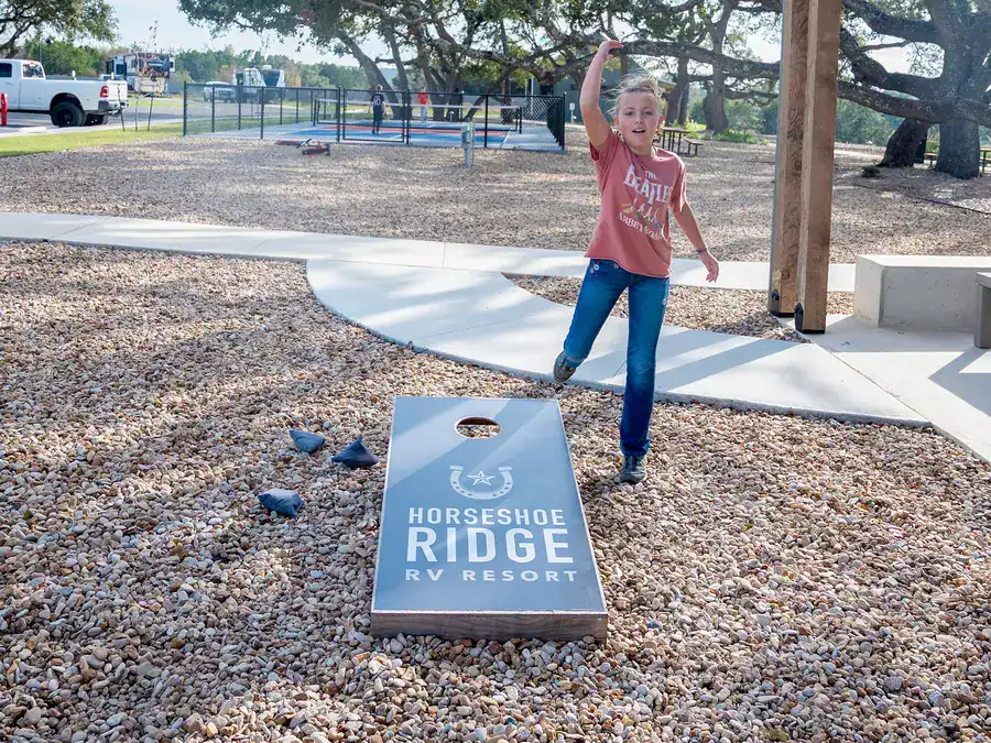Girl tossing a bag at a Horseshoe Ridge cornhole board beside the pavilion