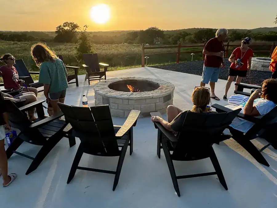 Guests gathered around a community fire pit as the sun sets over the Hill Country