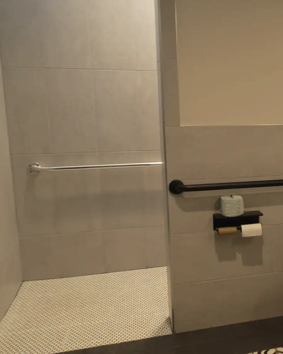 Curbless walk-in shower with gray tile walls and a white penny-tile floor in a bath house shower room