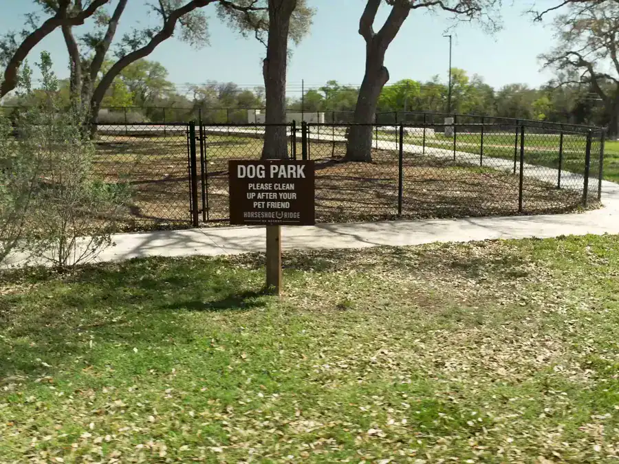 Fenced dog park and sign under live oak trees at Horseshoe Ridge