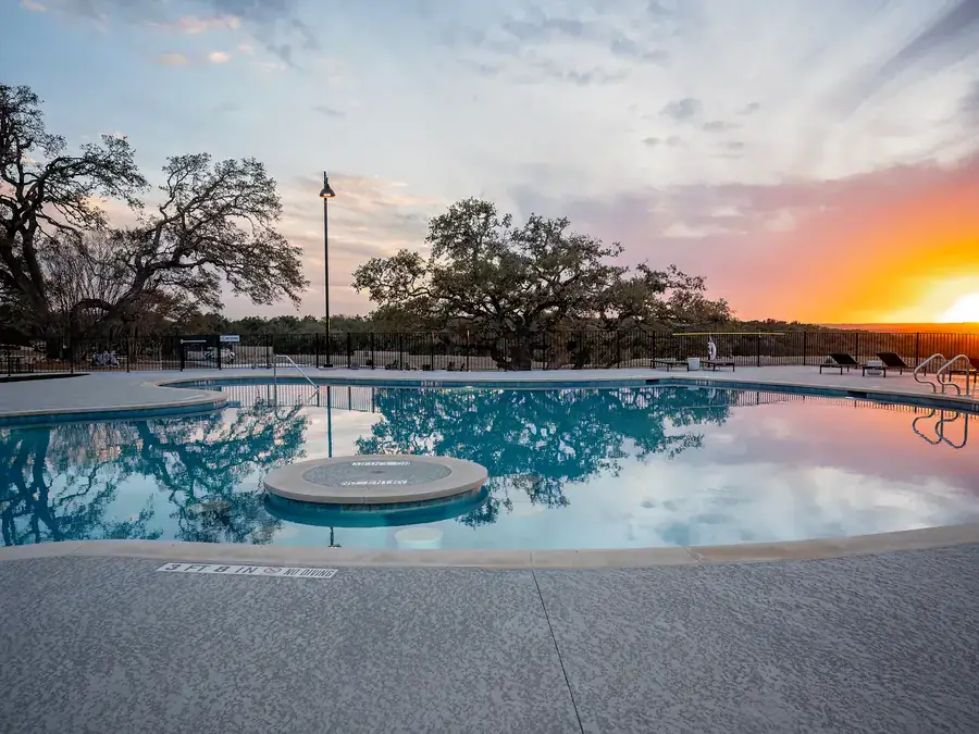 Resort pool with a swim-up table and deck at sunset, with live oaks reflected in the water