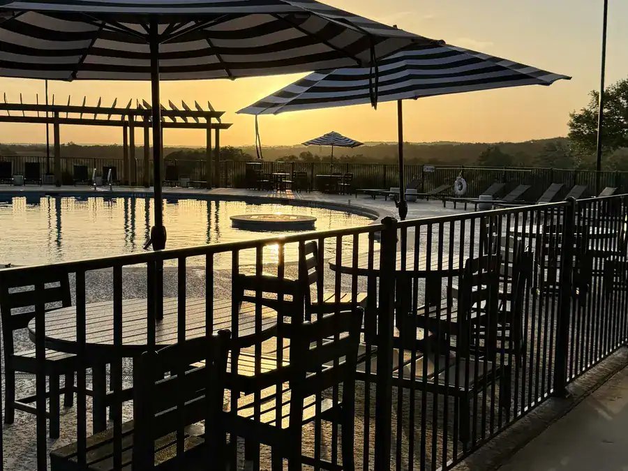 Pool deck tables and umbrellas at sunset, looking out over the pool and the Hill Country