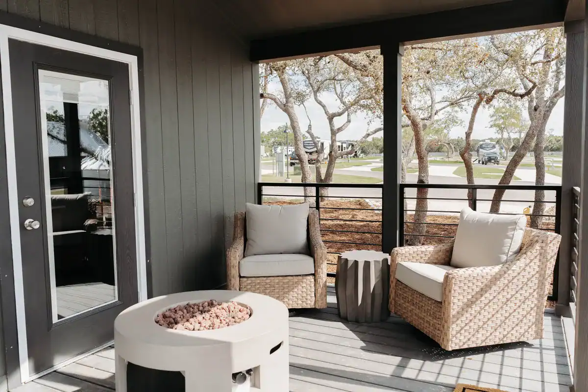 Secretariat cabin's front porch with wicker armchairs and a propane fire table under the oaks