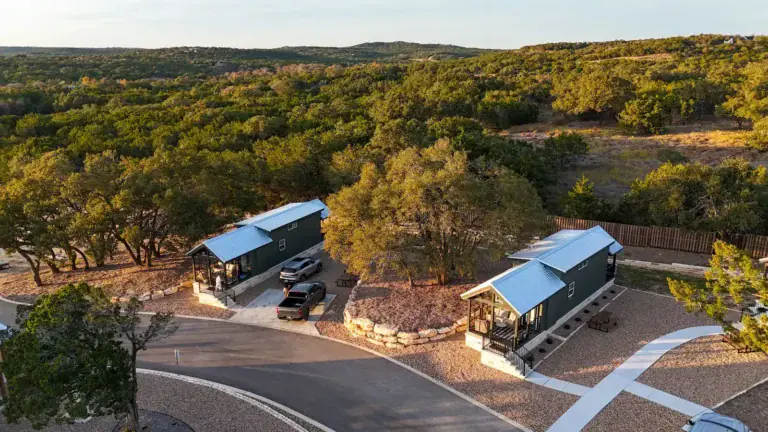 Golden-hour aerial of two cabins beside the oaks at Horseshoe Ridge RV Resort in Wimberley, Texas