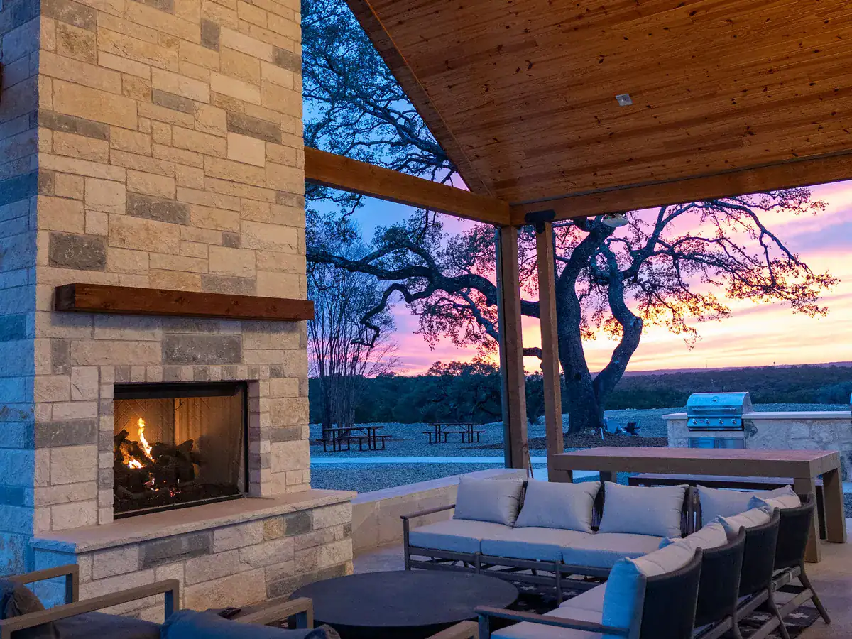 Covered pavilion with a stone fireplace and outdoor seating at dusk