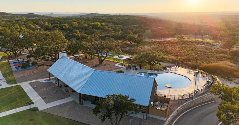 Aerial view of the Horseshoe Ridge clubhouse, pool and pickleball courts at sunset, with Texas Hill Country ridgelines beyond