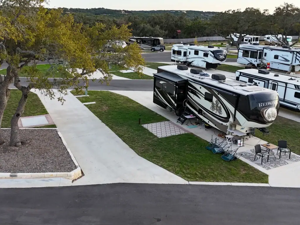 Fifth-wheel RV on a pull-through site with a patio, outdoor rug and chairs under a live oak at Horseshoe Ridge