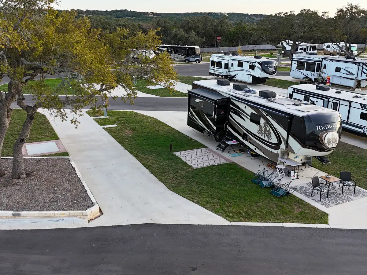 Fifth-wheel RV on a pull-through site with a patio, outdoor rug and chairs under a live oak at Horseshoe Ridge