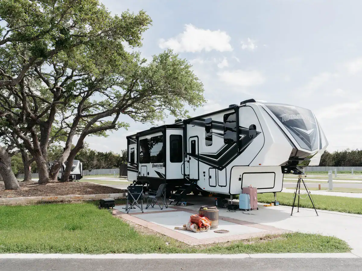 Fifth-wheel RV set up on a patio site under live oaks at Horseshoe Ridge, with the utility pedestal beside it