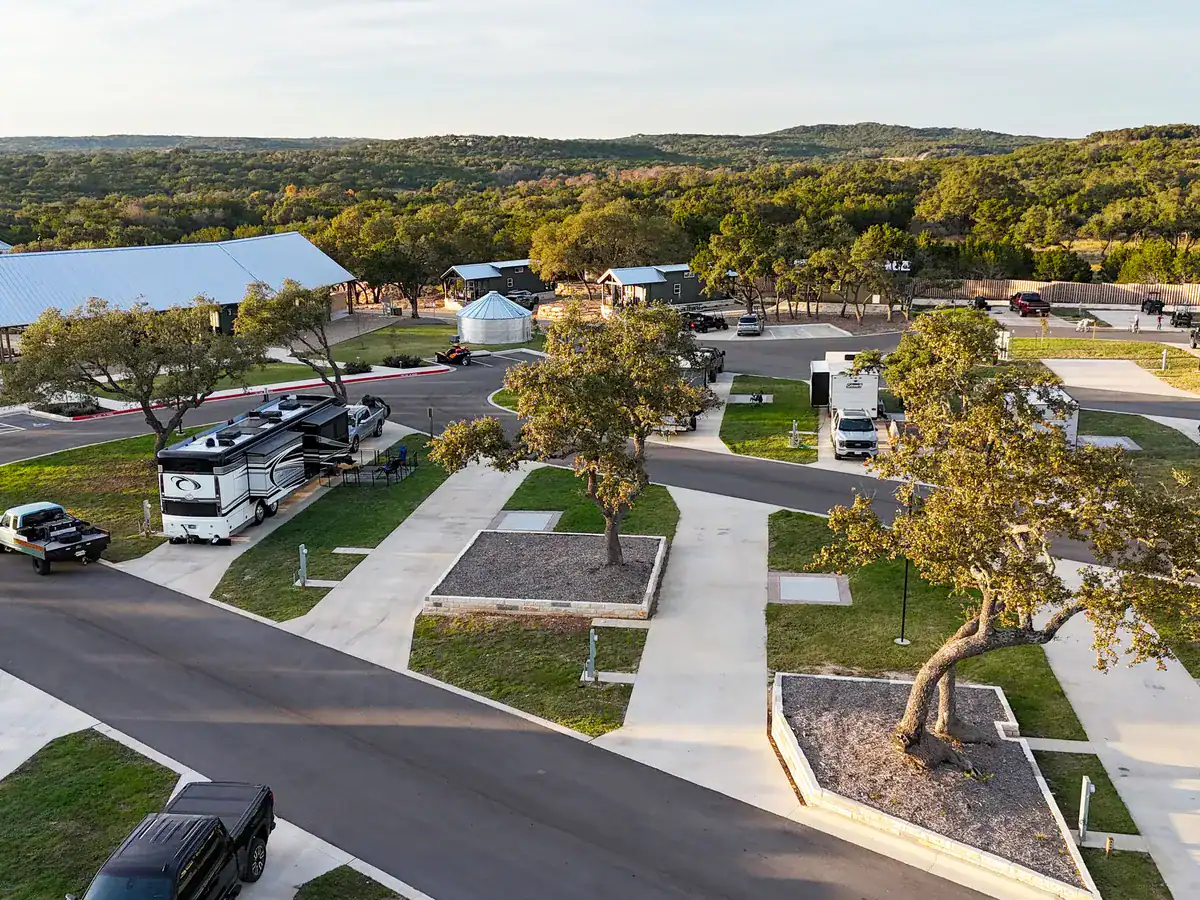 RV sites with concrete pads under live oaks at Horseshoe Ridge in Wimberley, with the clubhouse and Hill Country hills behind