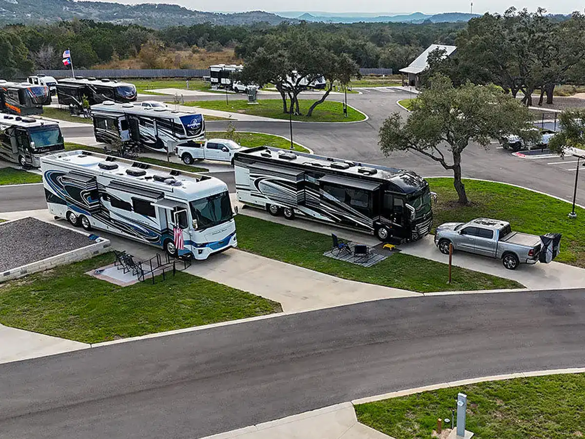 A Class A motorhome set up on a full-hookup concrete site among the oaks