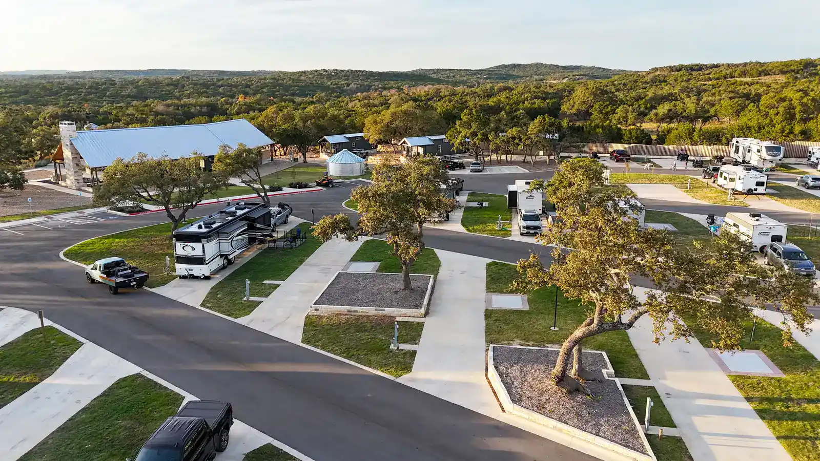 Golden-hour aerial of Horseshoe Ridge RV Resort: a Class A coach on its site, the clubhouse with its stone chimney, old oaks and the Hill Country ridgeline