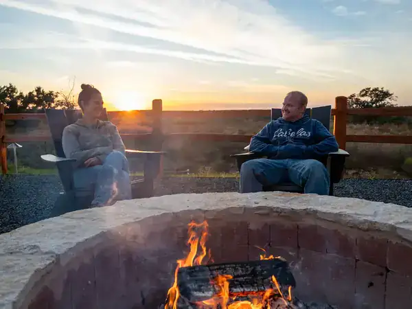 Two guests relaxing by the community fire pit at sunset