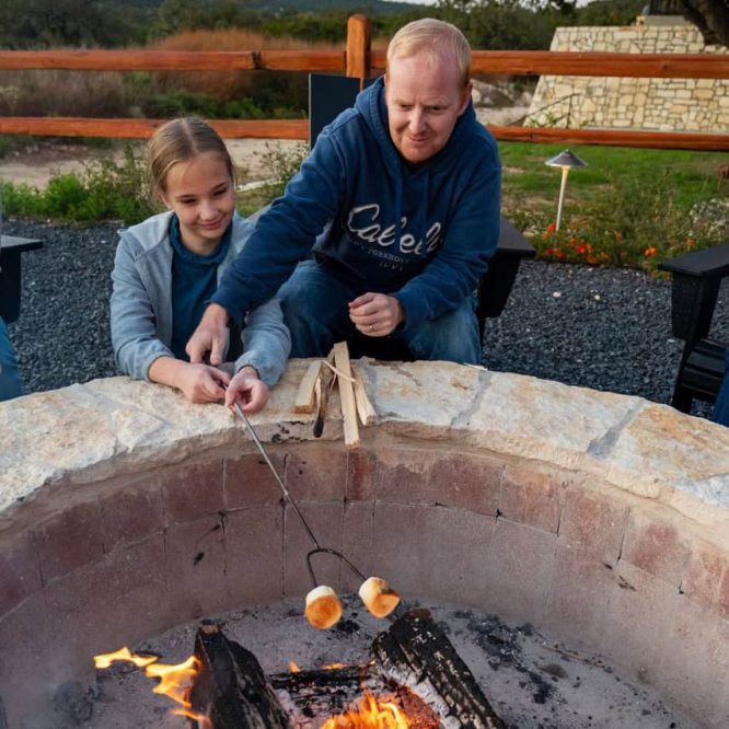 Father and daughter roasting marshmallows over a fire pit at Horseshoe Ridge RV.