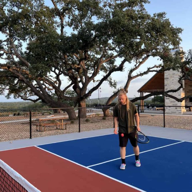 Young girl playing tennis on outdoor court at Horseshoe Ridge RV resort.