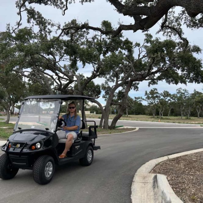 Golf cart on a paved road near large oak trees at Horseshoe Ridge RV resort.