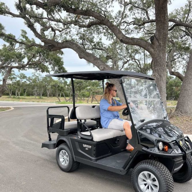 Woman riding a black golf cart under a large tree at Horseshoe Ridge RV.
